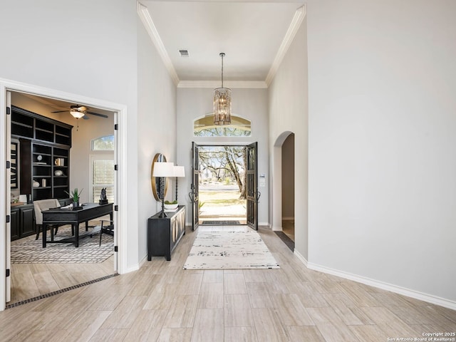 entryway featuring crown molding, a towering ceiling, ceiling fan, and light hardwood / wood-style flooring