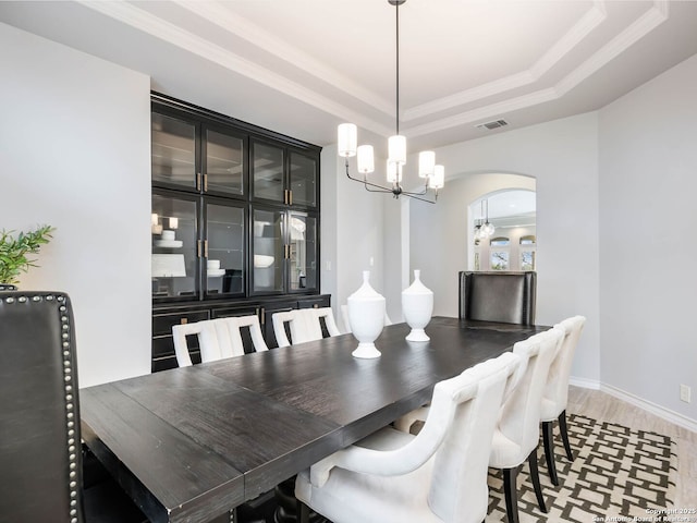 dining room with ornamental molding, a tray ceiling, a chandelier, and light hardwood / wood-style flooring