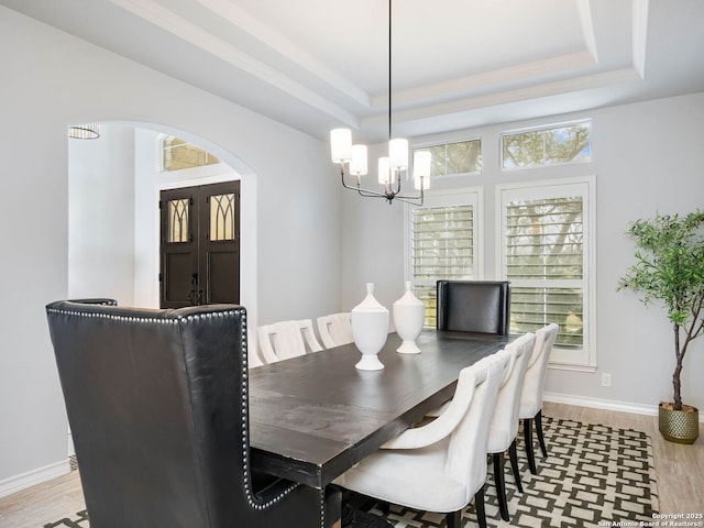 dining area with a raised ceiling, an inviting chandelier, and light hardwood / wood-style flooring