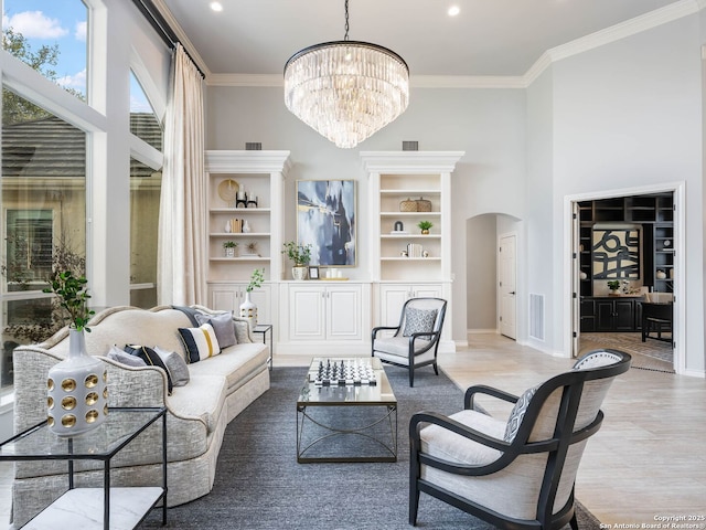 living room featuring ornamental molding, a towering ceiling, a chandelier, and light wood-type flooring