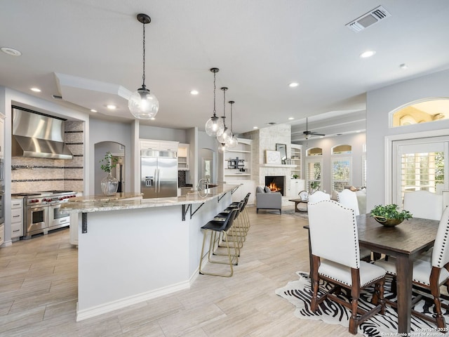 kitchen featuring wall chimney exhaust hood, white cabinetry, decorative light fixtures, premium appliances, and a large island