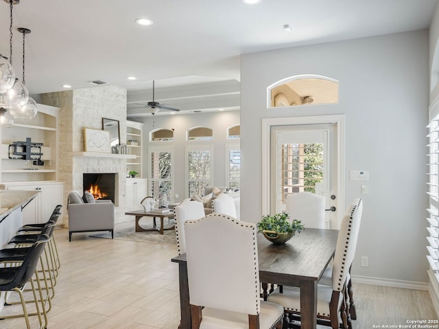 dining space with a stone fireplace, light hardwood / wood-style flooring, built in features, and ceiling fan