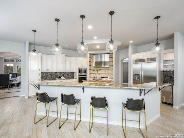 kitchen featuring a kitchen breakfast bar, built in appliances, decorative light fixtures, and light stone countertops