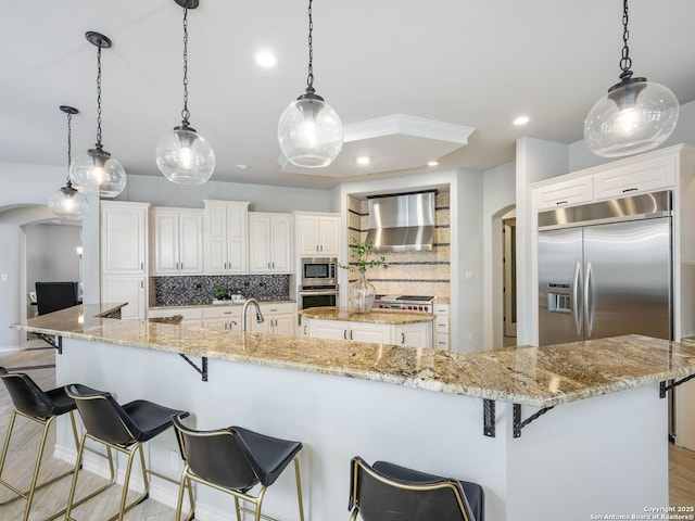 kitchen with built in appliances, wall chimney range hood, hanging light fixtures, and a spacious island