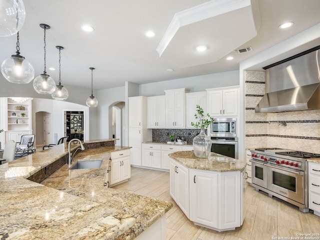 kitchen featuring white cabinetry, appliances with stainless steel finishes, wall chimney range hood, and a large island with sink