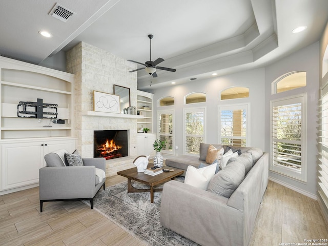 living room with a stone fireplace, ornamental molding, ceiling fan, light wood-type flooring, and built in shelves