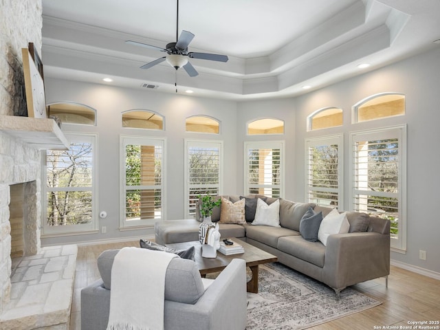 living room with ornamental molding, a tray ceiling, a stone fireplace, and a wealth of natural light