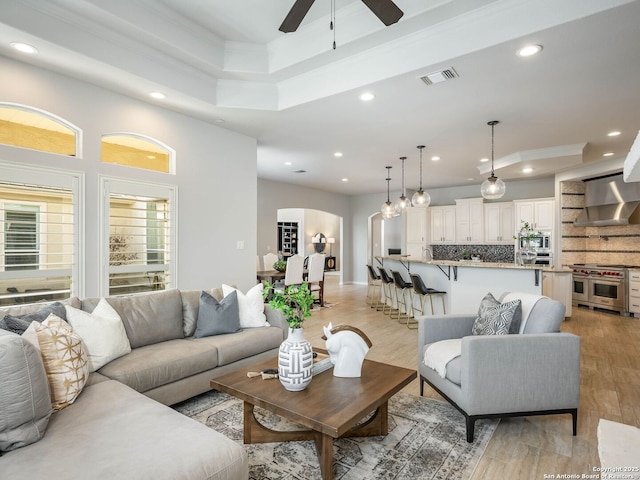 living room featuring ceiling fan, ornamental molding, a raised ceiling, and light wood-type flooring