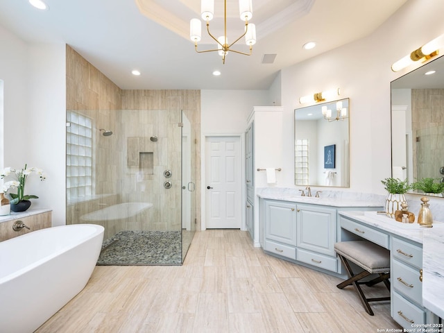 bathroom featuring a raised ceiling, shower with separate bathtub, a notable chandelier, and vanity