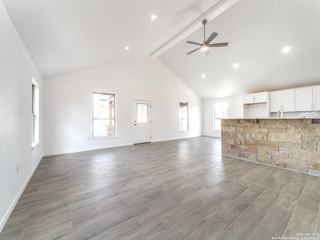 unfurnished living room with beamed ceiling, ceiling fan, high vaulted ceiling, and light wood-type flooring