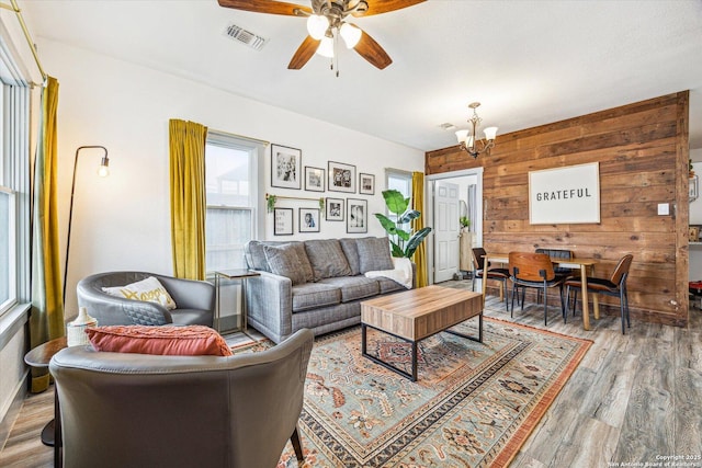 living room with wood-type flooring, ceiling fan with notable chandelier, and wood walls