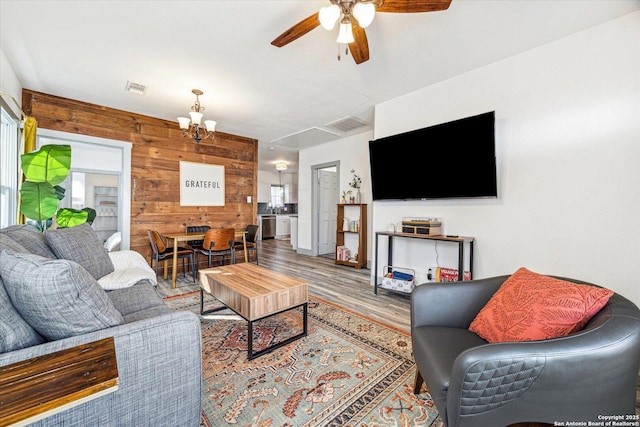 living room featuring hardwood / wood-style floors, ceiling fan with notable chandelier, and wooden walls