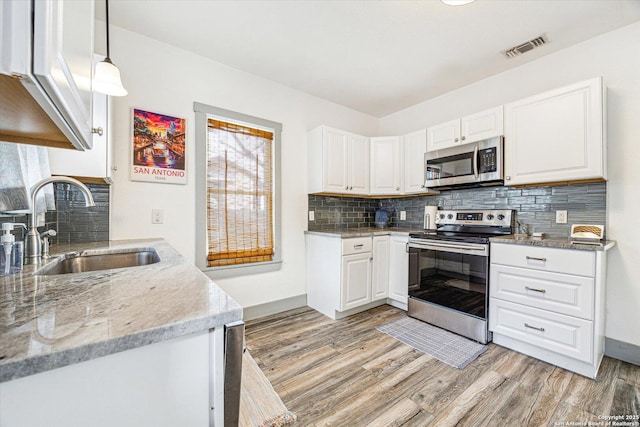 kitchen with pendant lighting, white cabinetry, sink, stainless steel appliances, and light stone countertops