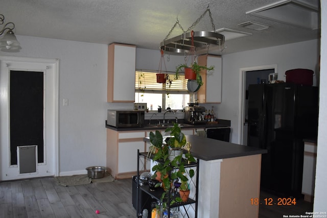 kitchen with sink, black refrigerator with ice dispenser, a textured ceiling, hardwood / wood-style flooring, and white cabinets