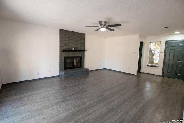 unfurnished living room with ceiling fan, dark hardwood / wood-style flooring, a brick fireplace, and a textured ceiling