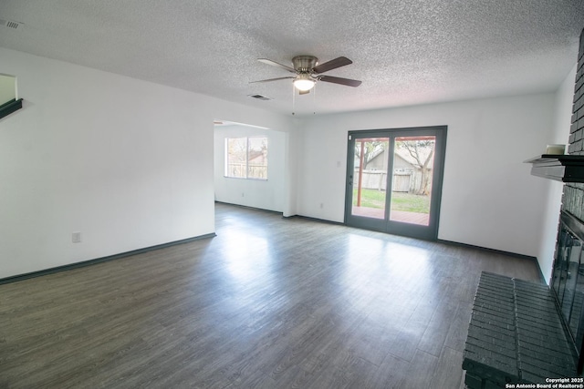 unfurnished living room with a brick fireplace, a textured ceiling, dark hardwood / wood-style floors, and ceiling fan