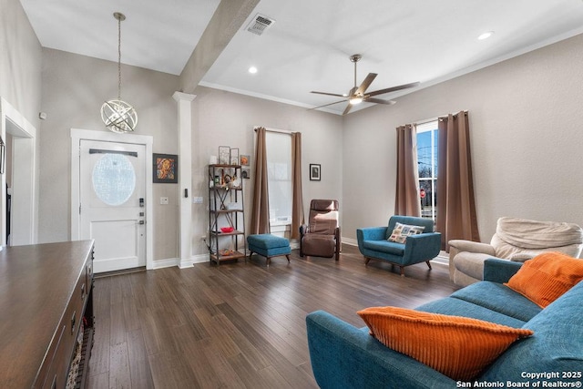 living room with crown molding, dark wood-type flooring, ceiling fan, and ornate columns