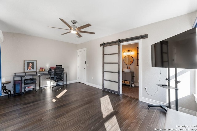 home office featuring dark wood-type flooring, ceiling fan, and a barn door