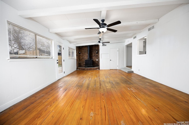 unfurnished living room with visible vents, beamed ceiling, hardwood / wood-style floors, baseboards, and a wood stove