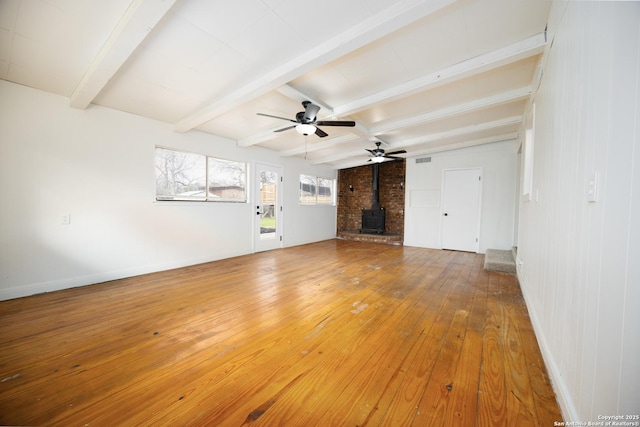 unfurnished living room with visible vents, baseboards, a wood stove, light wood-style floors, and beamed ceiling