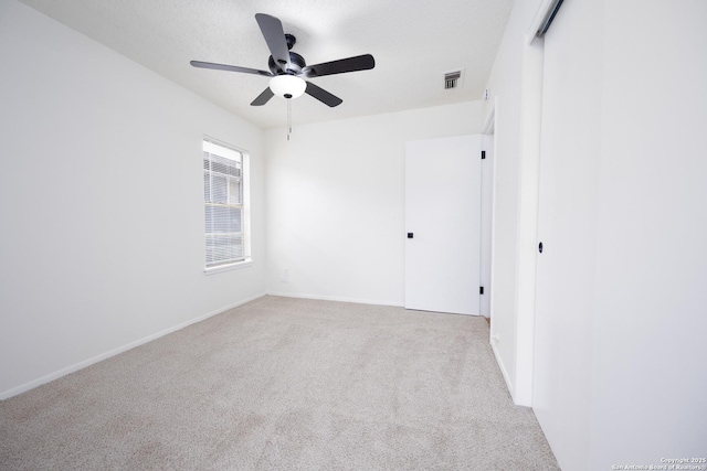 carpeted empty room featuring baseboards, visible vents, a textured ceiling, and ceiling fan