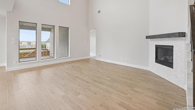 305 Hulda Trl, New Braunfels, TX 78130 - unfurnished living room featuring light wood-type flooring, a towering ceiling, a glass covered fireplace, and baseboards