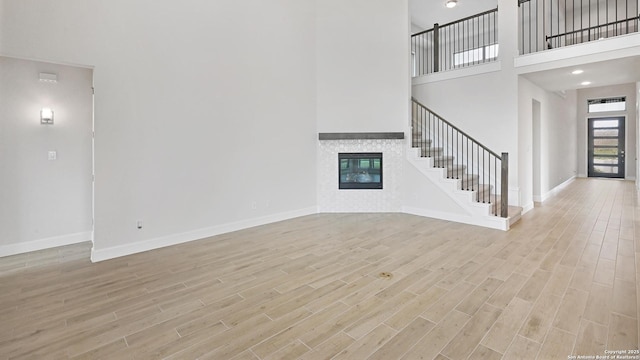 305 Hulda Trl, New Braunfels, TX 78130 - unfurnished living room with stairs, light wood-type flooring, a towering ceiling, a glass covered fireplace, and baseboards