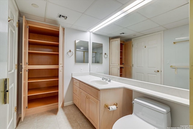 bathroom with a drop ceiling, vanity, tile patterned floors, and toilet