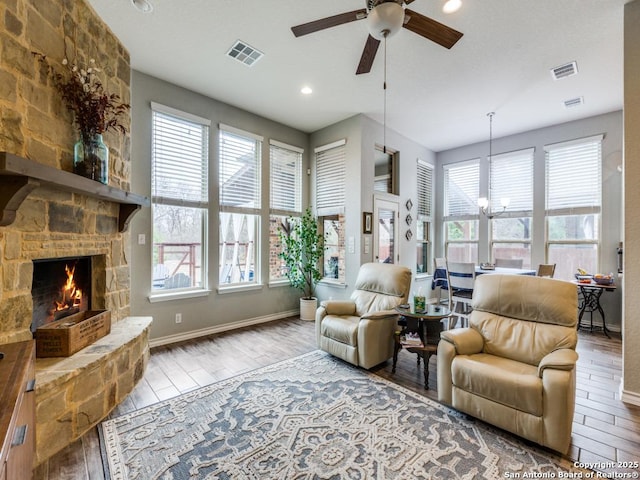 living room with ceiling fan with notable chandelier, a fireplace, plenty of natural light, and light wood-type flooring