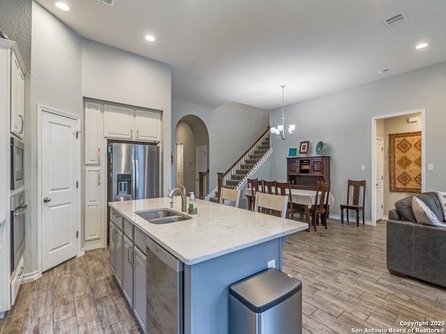 kitchen featuring appliances with stainless steel finishes, decorative light fixtures, an island with sink, sink, and light hardwood / wood-style floors