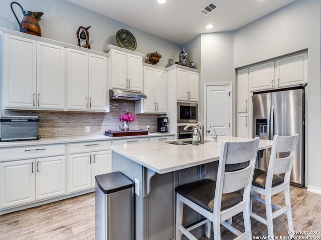 kitchen with built in microwave, an island with sink, sink, white cabinets, and stainless steel fridge with ice dispenser