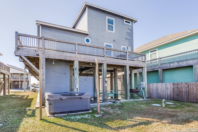 rear view of property with a hot tub, a deck, and a lawn