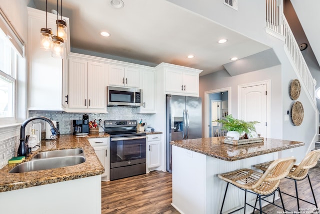 kitchen with sink, appliances with stainless steel finishes, a kitchen island, pendant lighting, and white cabinets