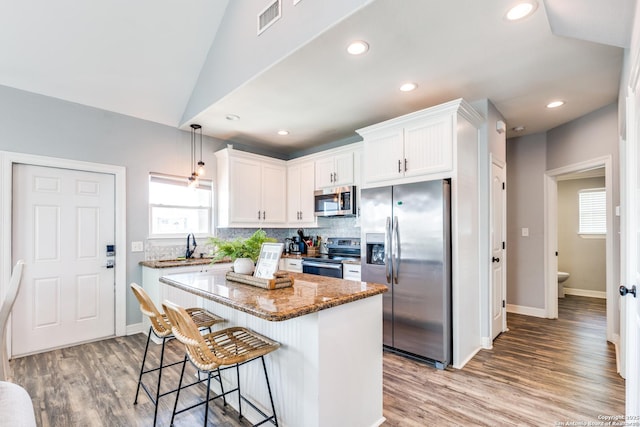 kitchen with white cabinetry, hanging light fixtures, appliances with stainless steel finishes, a kitchen island, and dark stone counters