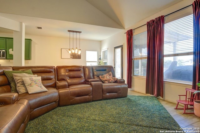 living room featuring vaulted ceiling, a healthy amount of sunlight, a notable chandelier, and light wood-type flooring