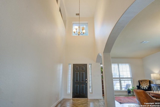 entryway with parquet flooring, a towering ceiling, and an inviting chandelier