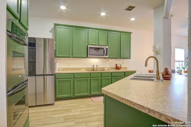 kitchen with green cabinets, stainless steel appliances, sink, and light wood-type flooring