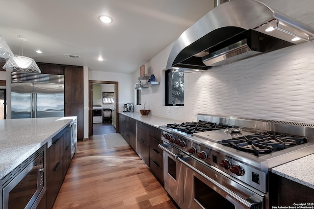 kitchen featuring island exhaust hood, dark brown cabinetry, built in appliances, and decorative light fixtures