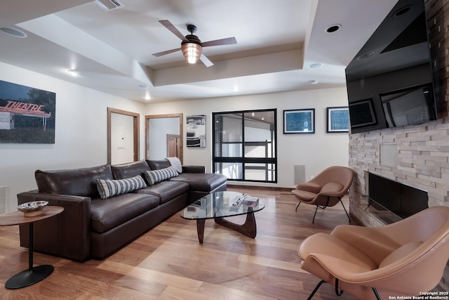 living room with ceiling fan, a fireplace, a tray ceiling, and light hardwood / wood-style floors