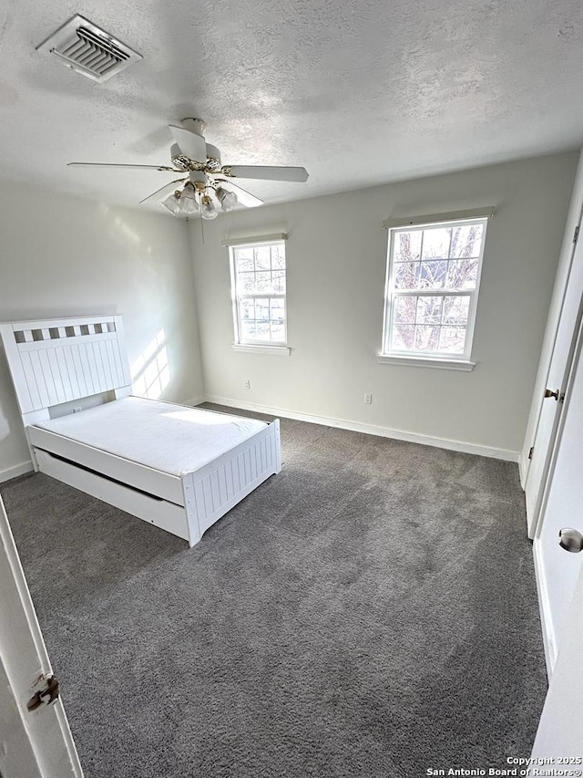 unfurnished bedroom featuring ceiling fan, a textured ceiling, and dark colored carpet