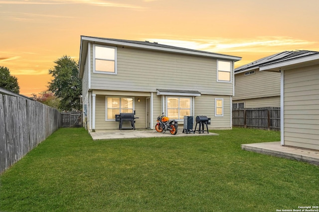 back house at dusk featuring a patio area and a lawn