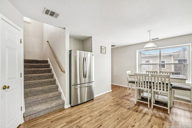 kitchen featuring light hardwood / wood-style flooring, decorative light fixtures, stainless steel fridge, and a textured ceiling