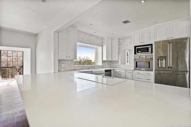 kitchen featuring appliances with stainless steel finishes, white cabinetry, decorative backsplash, kitchen peninsula, and dark wood-type flooring