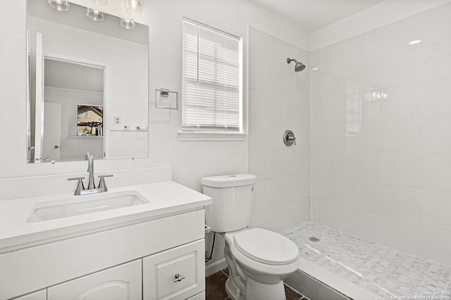 bathroom featuring vanity, a tile shower, and toilet