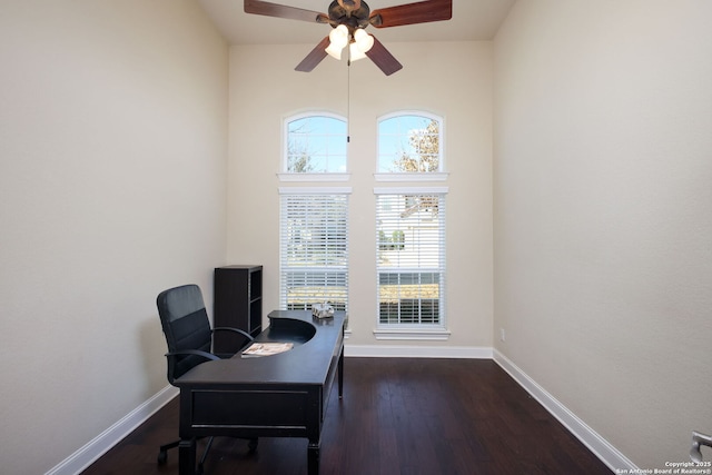 office with dark hardwood / wood-style flooring, a towering ceiling, and ceiling fan