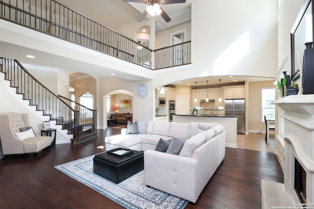 living room with a towering ceiling, ornamental molding, ceiling fan, a high end fireplace, and dark wood-type flooring