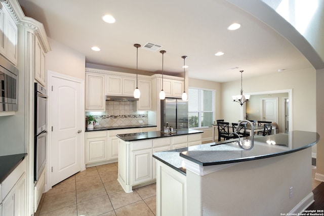 kitchen with tasteful backsplash, hanging light fixtures, a center island with sink, light tile patterned floors, and appliances with stainless steel finishes