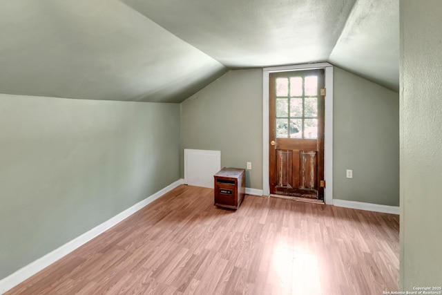 additional living space featuring vaulted ceiling, a textured ceiling, and light hardwood / wood-style flooring