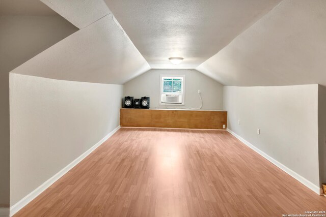 additional living space featuring cooling unit, vaulted ceiling, light hardwood / wood-style floors, and a textured ceiling