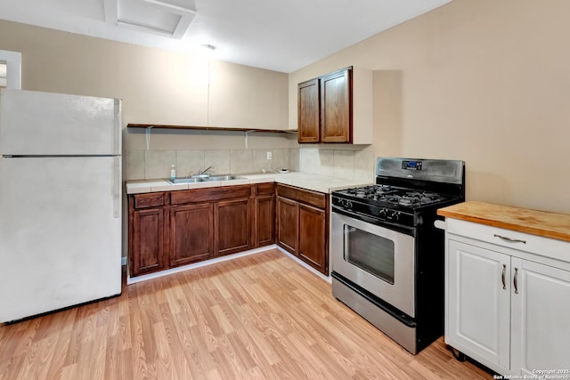 kitchen featuring sink, gas stove, tasteful backsplash, white fridge, and light hardwood / wood-style floors